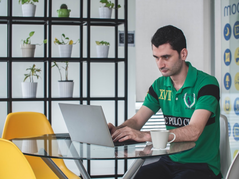 man sitting on gray metal chair while using gray laptop computer