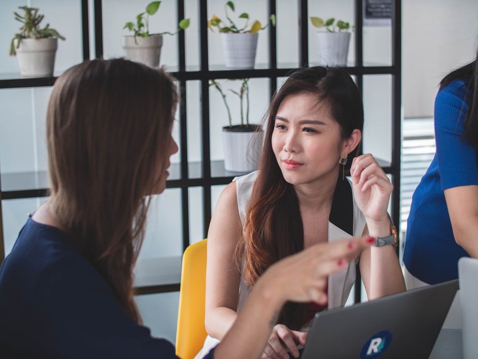 Two women sit across from each other in an office space while talking.