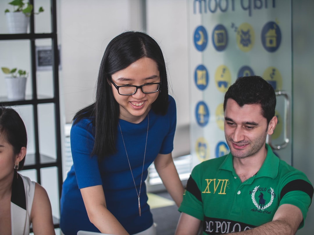smiling woman standing beside smiling man pointing MacBook,