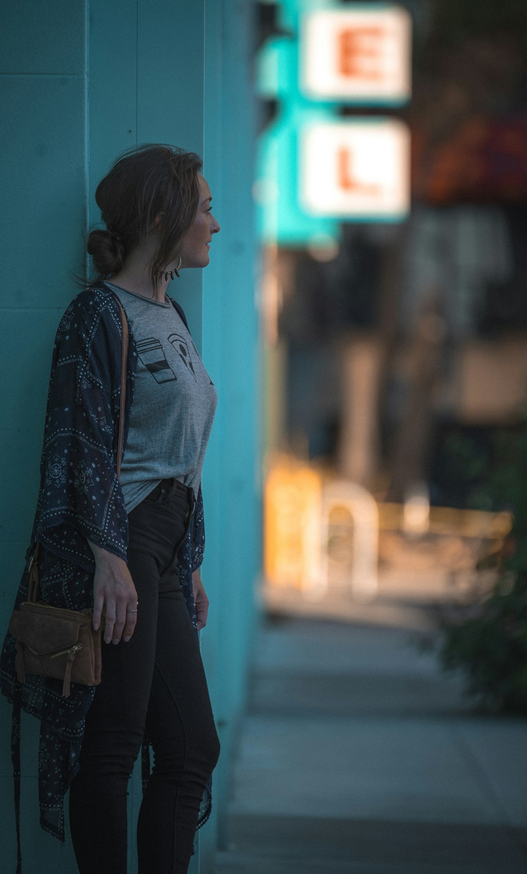 woman wearing gray denim jeans standing beside teal painted wall looking at tree selective focus photography