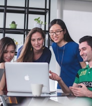 four people watching on white MacBook on top of glass-top table