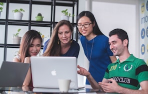 four people watching on white MacBook on top of glass-top table