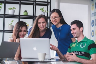 four people watching on white MacBook on top of glass-top table