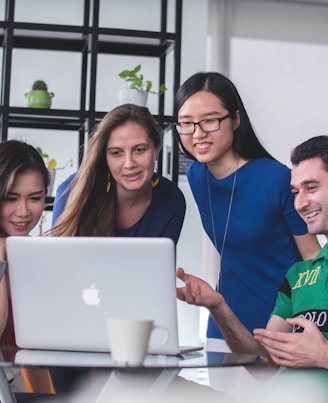 four people watching on white MacBook on top of glass-top table