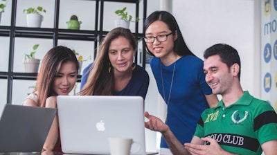 four people watching on white MacBook on top of glass-top table