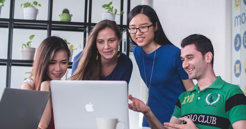 four people watching on white MacBook on top of glass-top table