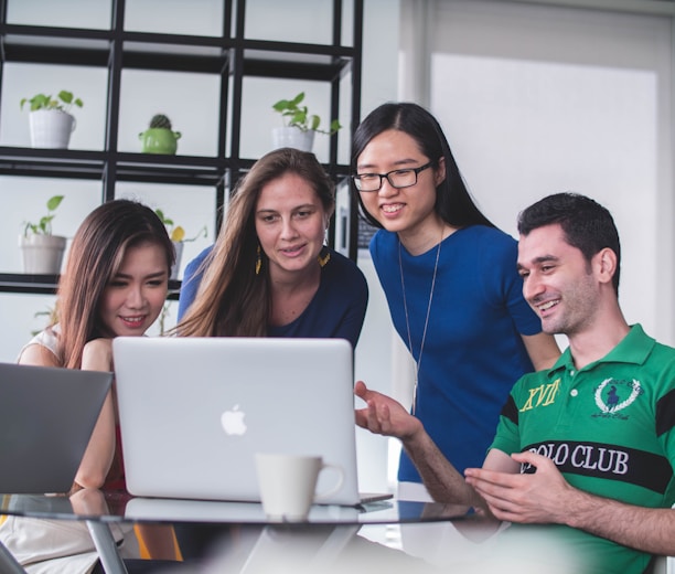 four people watching on white MacBook on top of glass-top table