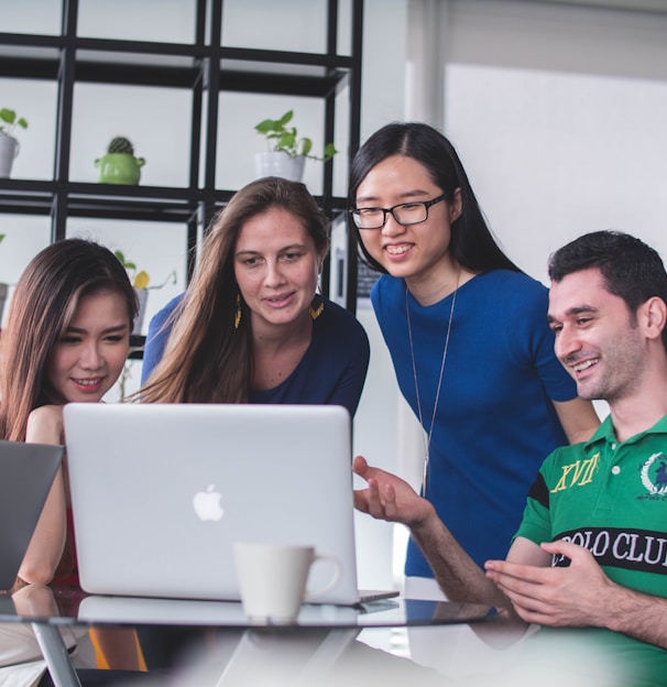 four people watching on white MacBook on top of glass-top table