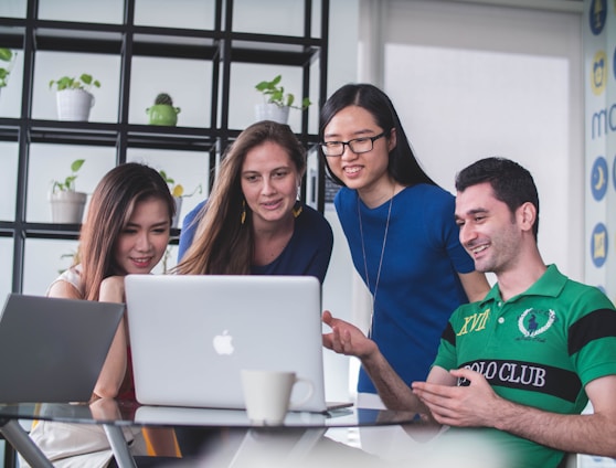 four people watching on white MacBook on top of glass-top table