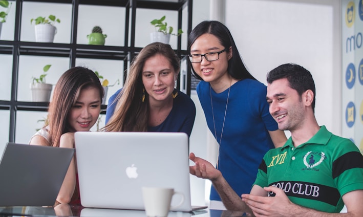 four people watching on white MacBook on top of glass-top table