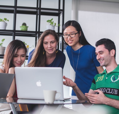 four people watching on white MacBook on top of glass-top table