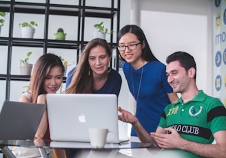 four people watching on white MacBook on top of glass-top table