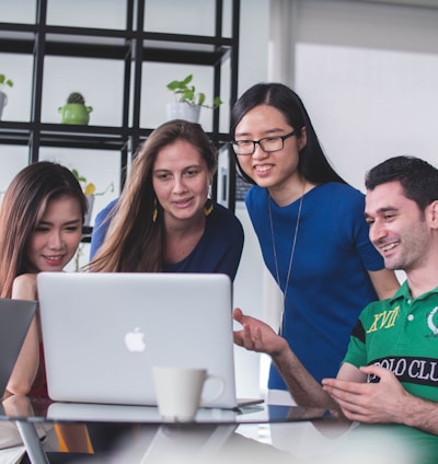 four people watching on white MacBook on top of glass-top table