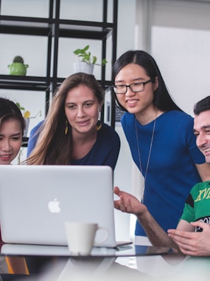 four people watching on white MacBook on top of glass-top table