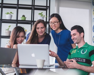 four people watching on white MacBook on top of glass-top table