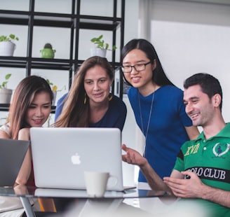 four people watching on white MacBook on top of glass-top table