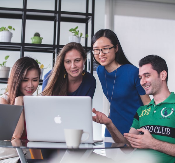 four people watching on white MacBook on top of glass-top table