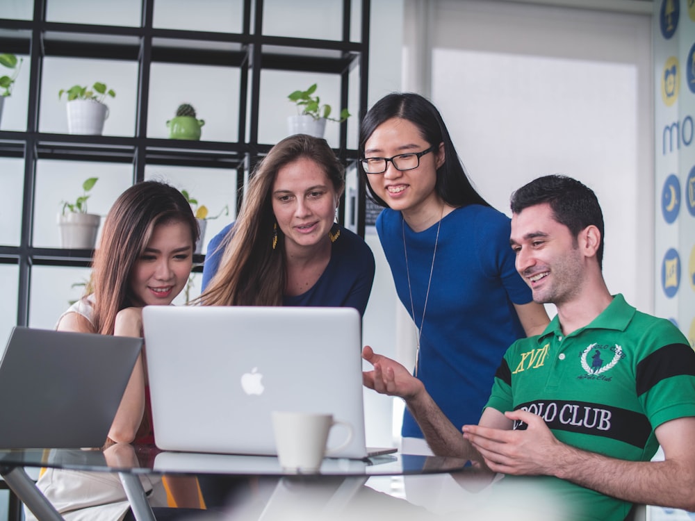 quatro pessoas assistindo no MacBook branco em cima da mesa de vidro