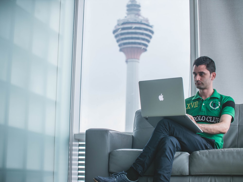 man sitting on sofa holding MacBook