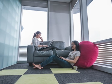 A man and woman working closely on laptops in a sleek high-rise office with sunset light streaming through large windows.