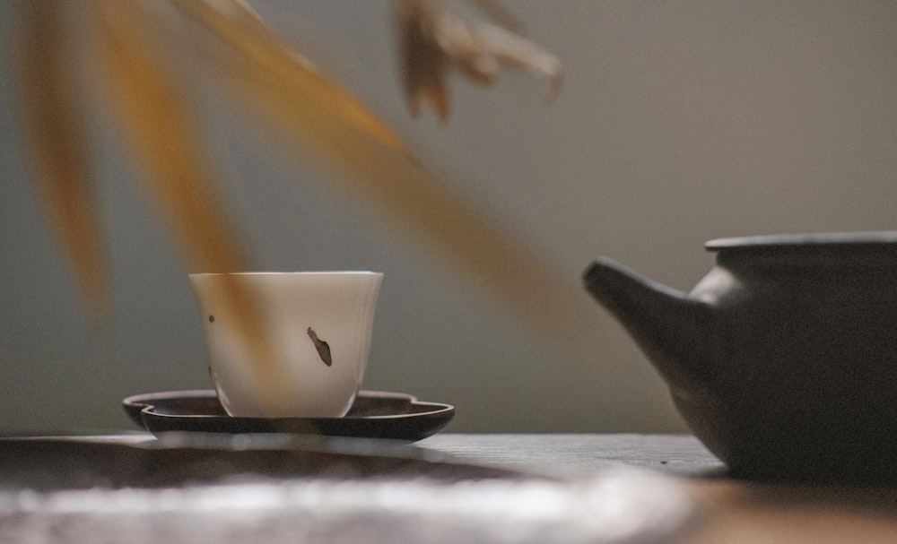 tazza da tè bianca su piattino nero vicino a teiera nera