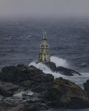 An abandoned lighthouse standing tall against a dark, stormy ocean backdrop.