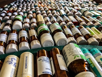 Rows of small bottles with white caps and labels, possibly containing homeopathic remedies, are arranged in a neatly organized manner on a green surface.