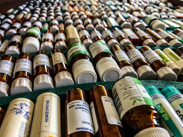 Rows of small bottles with white caps and labels, possibly containing homeopathic remedies, are arranged in a neatly organized manner on a green surface.