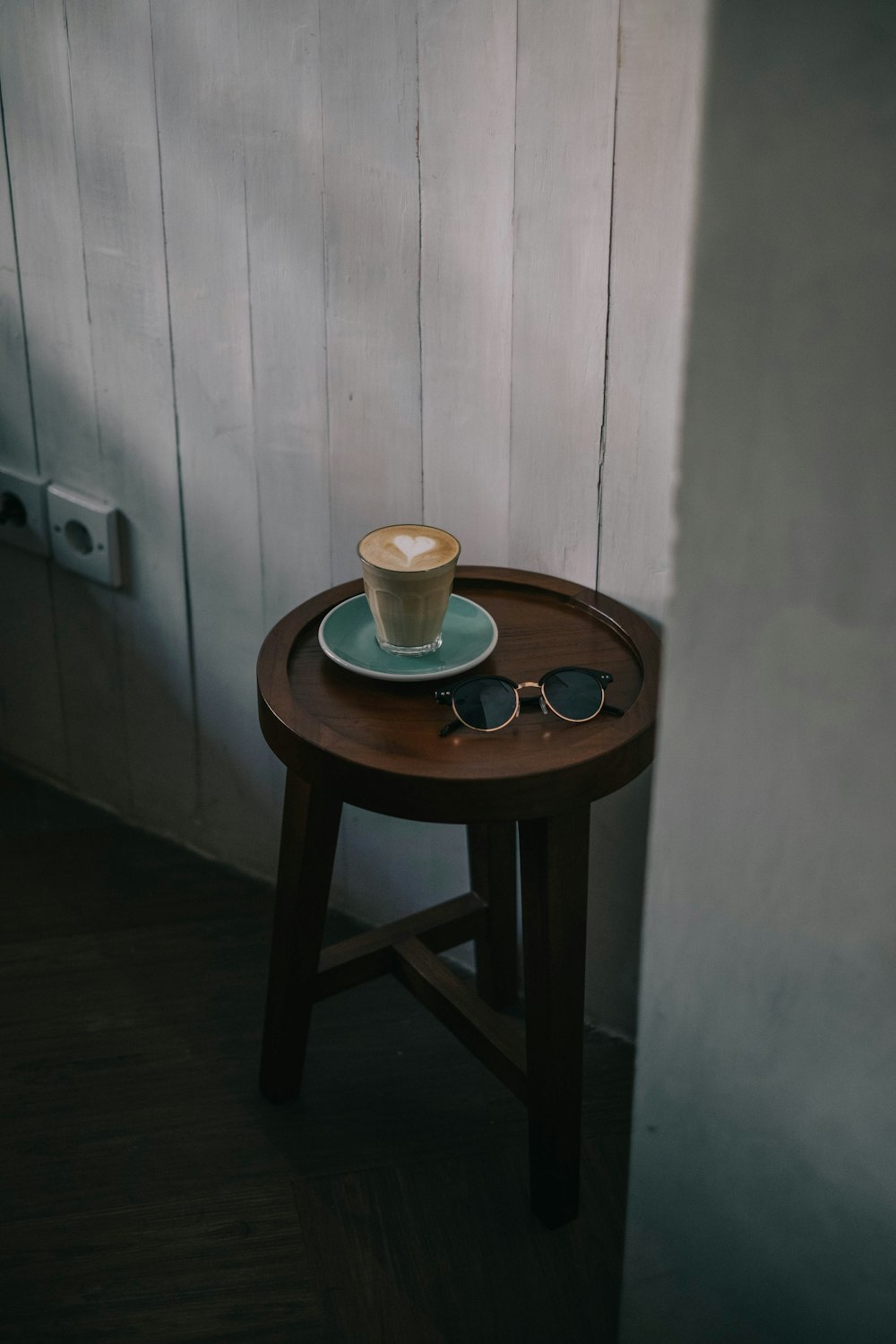 café com leite com arte do coração na mesa final de madeira marrom ao lado de óculos de sol pretos