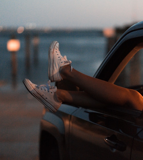 selective focus photography of person wearing white low-top sneakers inside vehicle