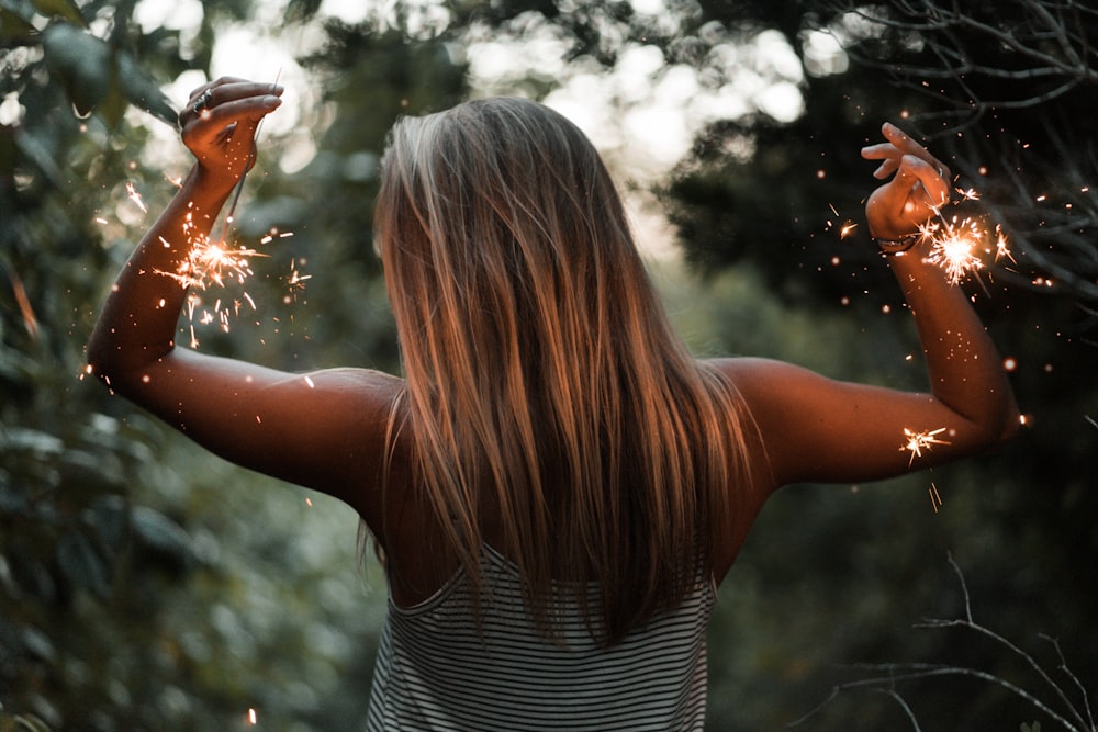 woman holding sparklers between bushes