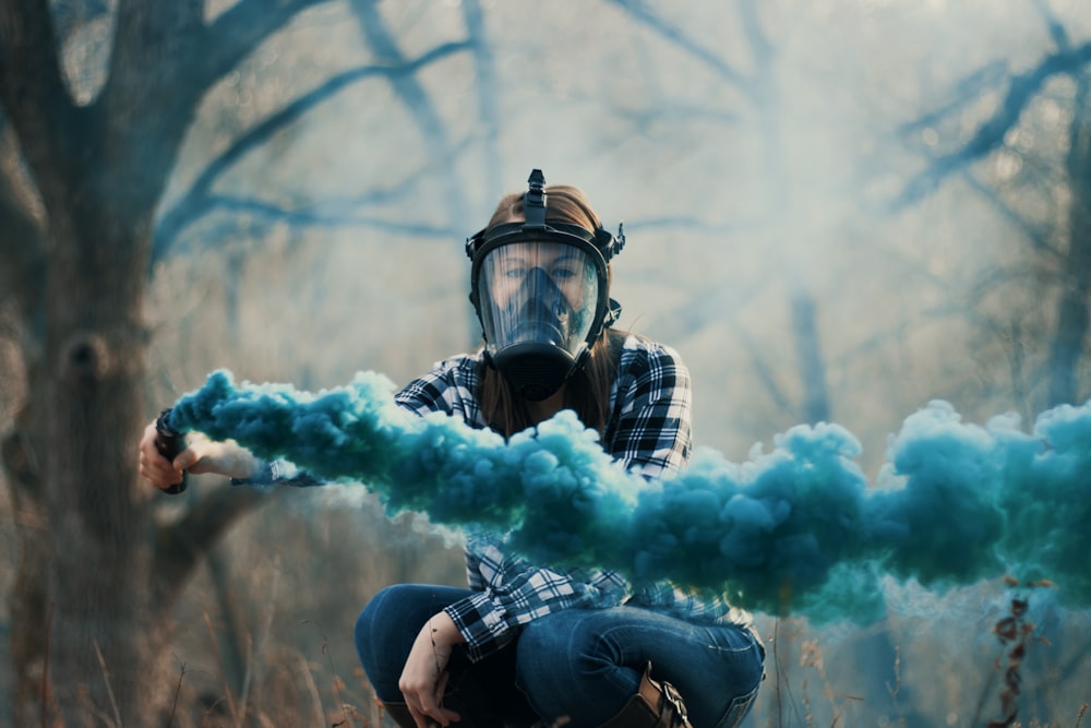person wearing black gas mask while using blue smoke