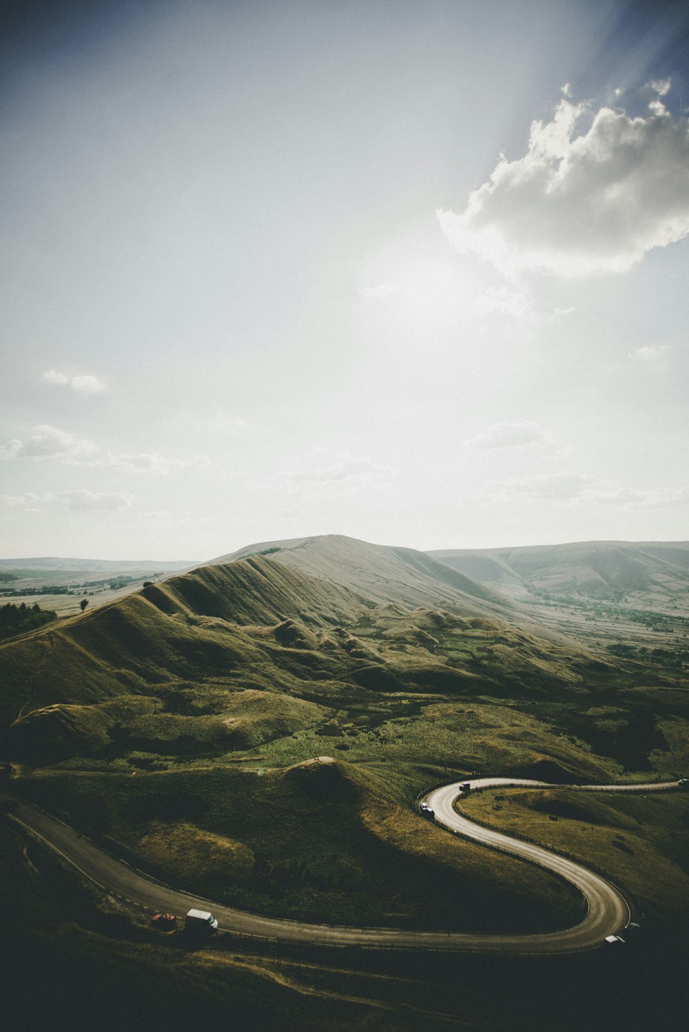 aerial photography of vehicle arriving on concrete road near mountains under white clouds at daytime