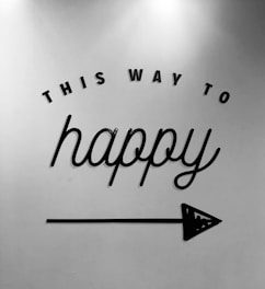 Black text on a white background reads 'This Way to Happy' with an arrow pointing to the right. The text has a cheerful, cursive style with a simple, minimalist design.