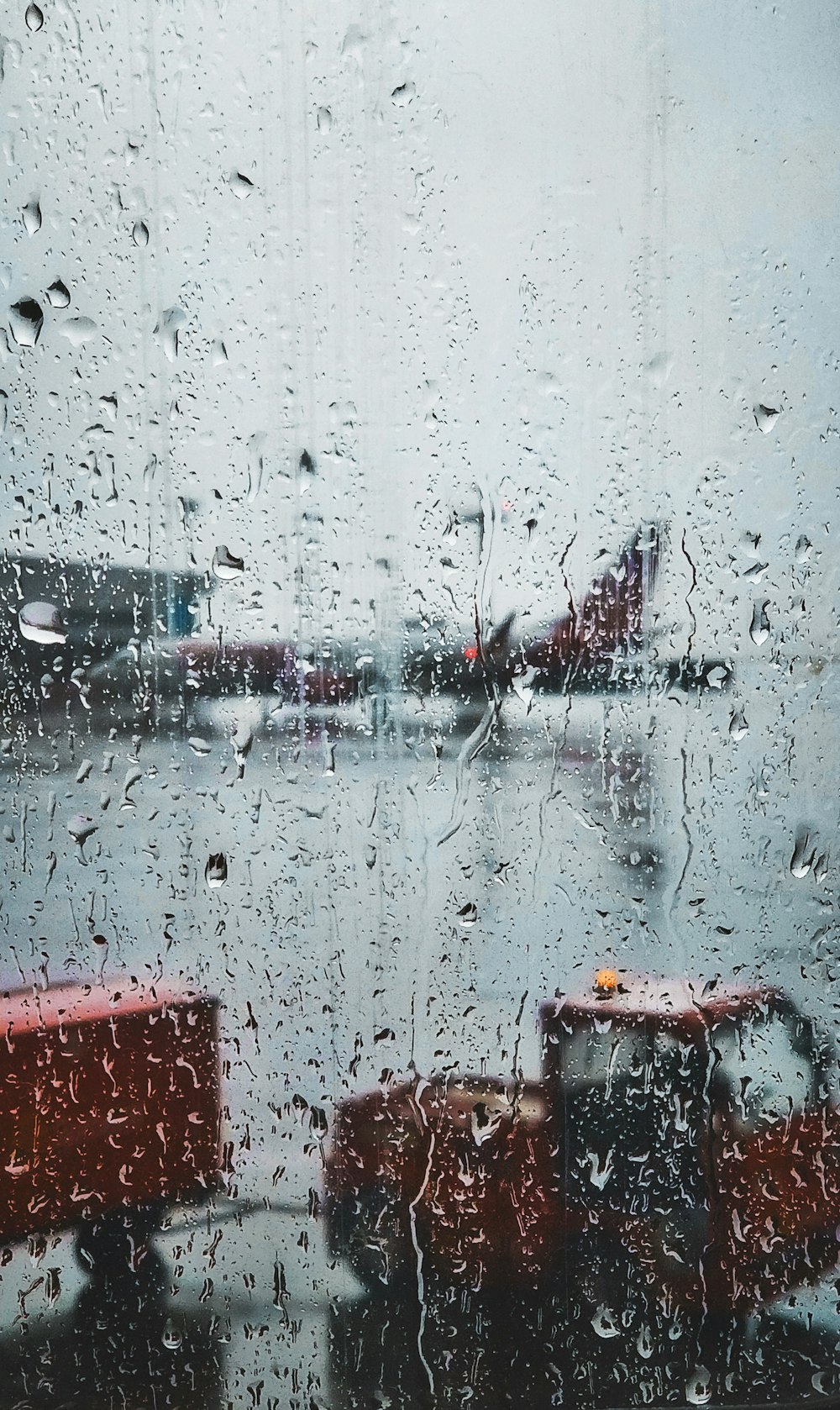 selective focus photography of glass panel with raindrops with view of commuter plane