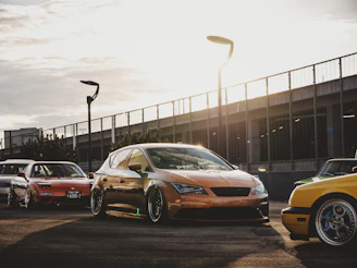 Wide shot of a car meet at dusk, rows of modified trucks and supercars under string lights.