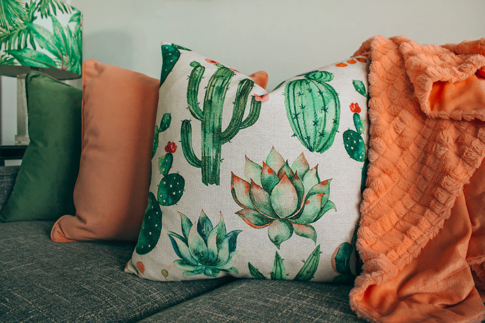 Three decorative throw pillows in green, orange, and white patterns styled on a sofa