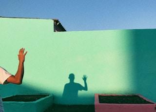 person waving reflecting shadow on teal wall paint