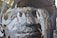 A close-up of a metal sculpture with abstract cutout patterns and a rusty texture. The sculpture is composed of layered metal pieces, with some areas showing weathered rust and others painted in a matte gray. The background is slightly blurred, focusing attention on the intricate details and industrial feel of the artwork.