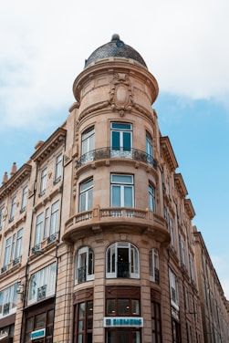 A historic building with detailed architectural features, including ornate stonework, large windows, and a round corner tower topped with a dome. The building has a classic European design, with a prominent sign indicating a Siemens store on the ground floor.