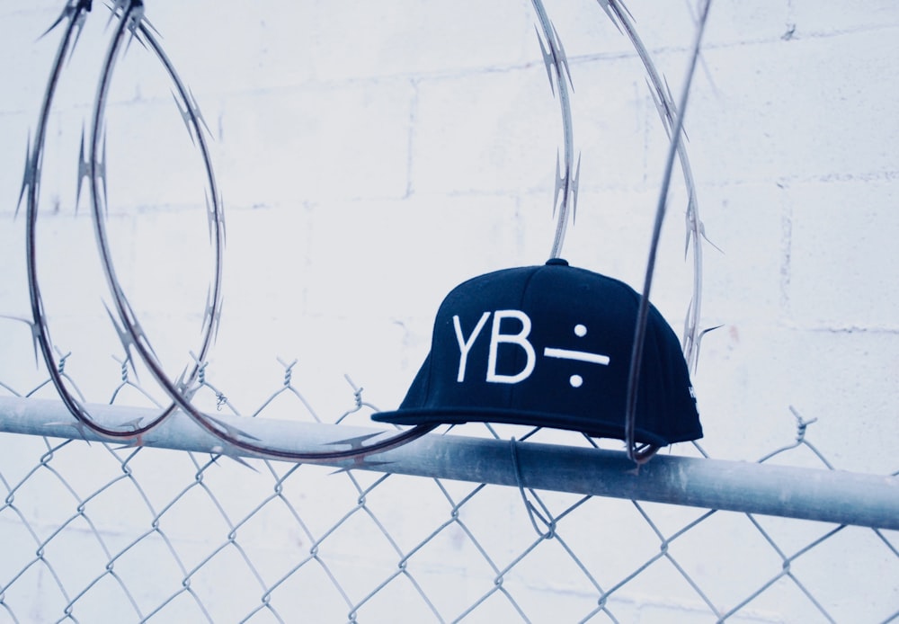 black YB fitted cap on gray cyclone fences