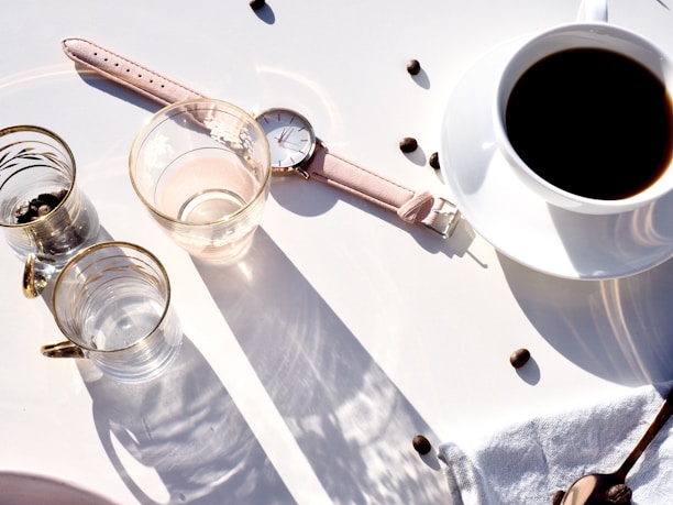 Minimalist coffee cup on a white table with a perfume bottle and design magazines nearby