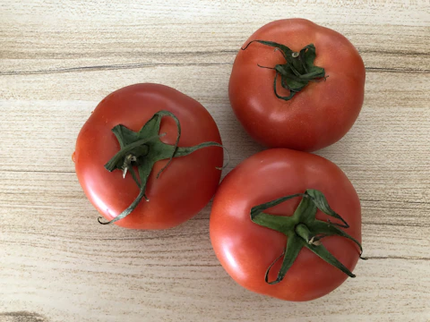 Close-up of ripe crimson tomatoes on a textured wooden table, bathed in natural light.