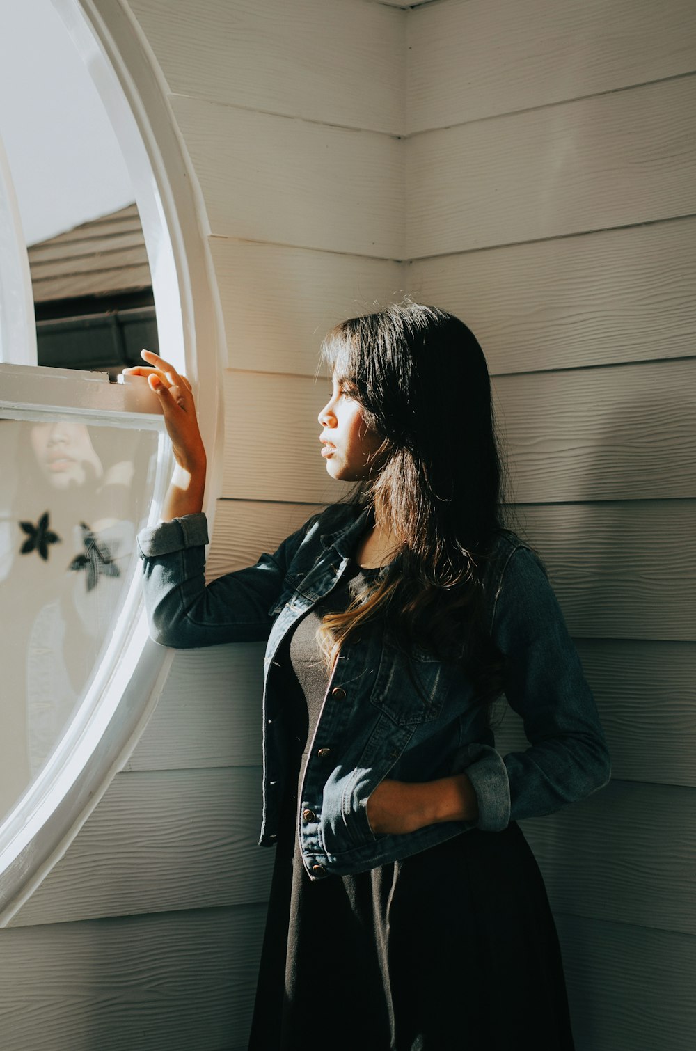 woman in blue denim jacket standing beside window