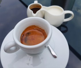 A close-up of a glass coffee cup filled with rich espresso, resting on a saucer.