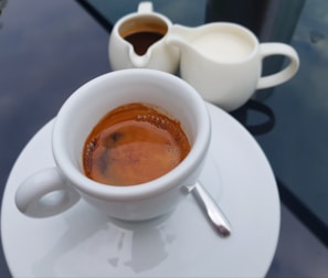 A close-up of a glass coffee cup filled with rich espresso, resting on a saucer.
