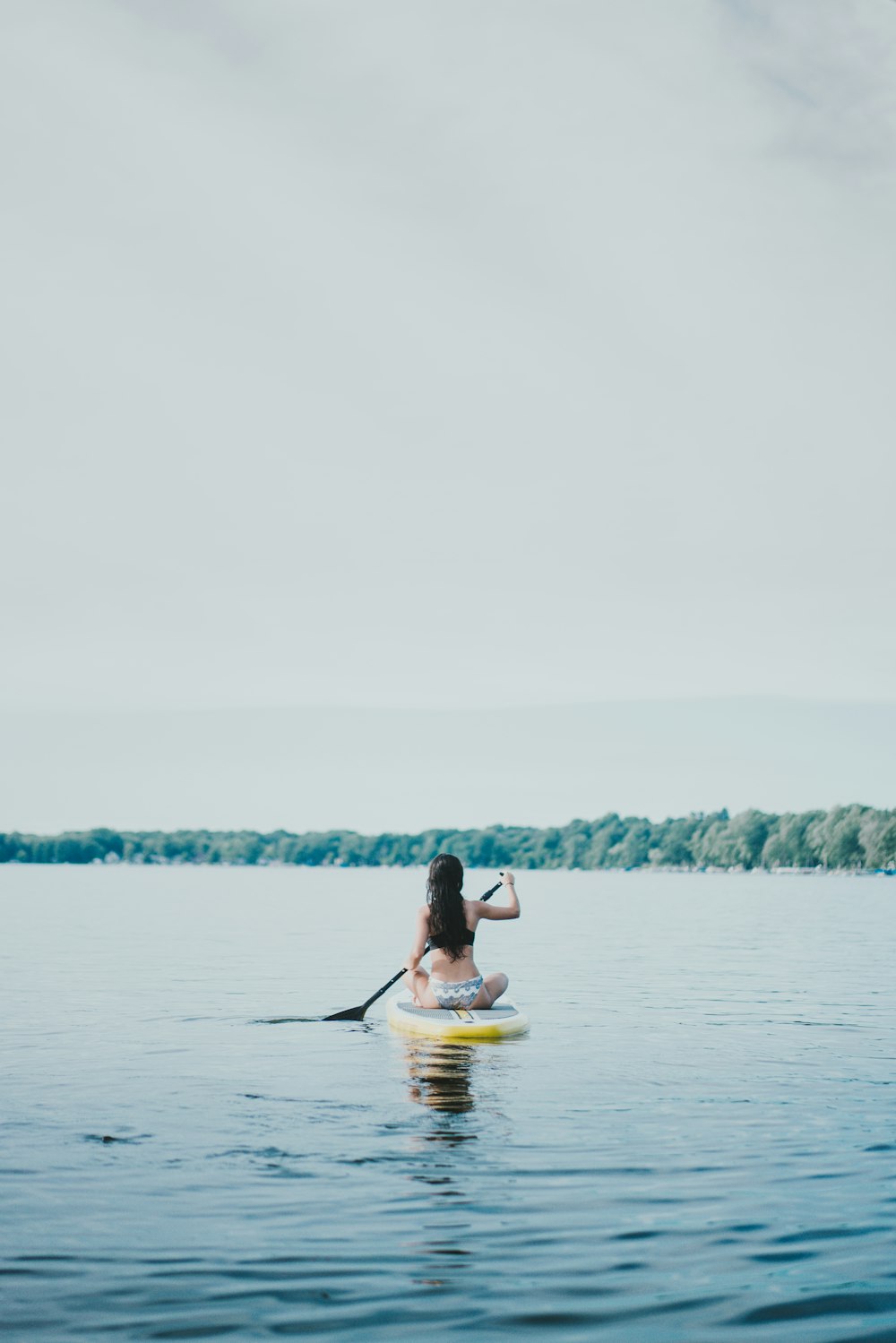 Donna che si siede sulla tavola da paddle gialla durante il giorno