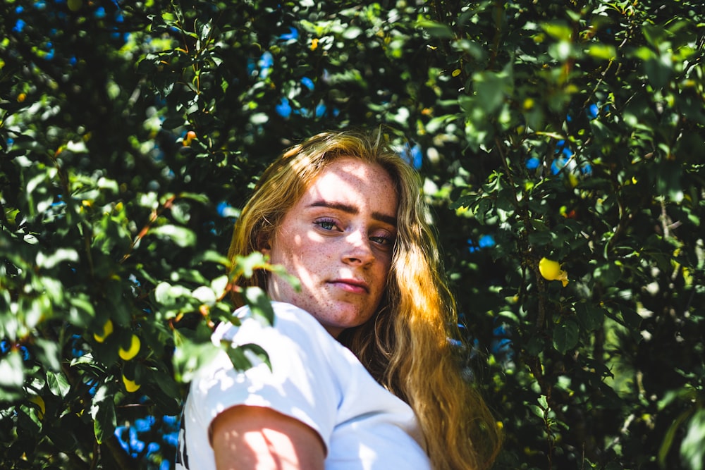 woman wearing white top under green leafed plant