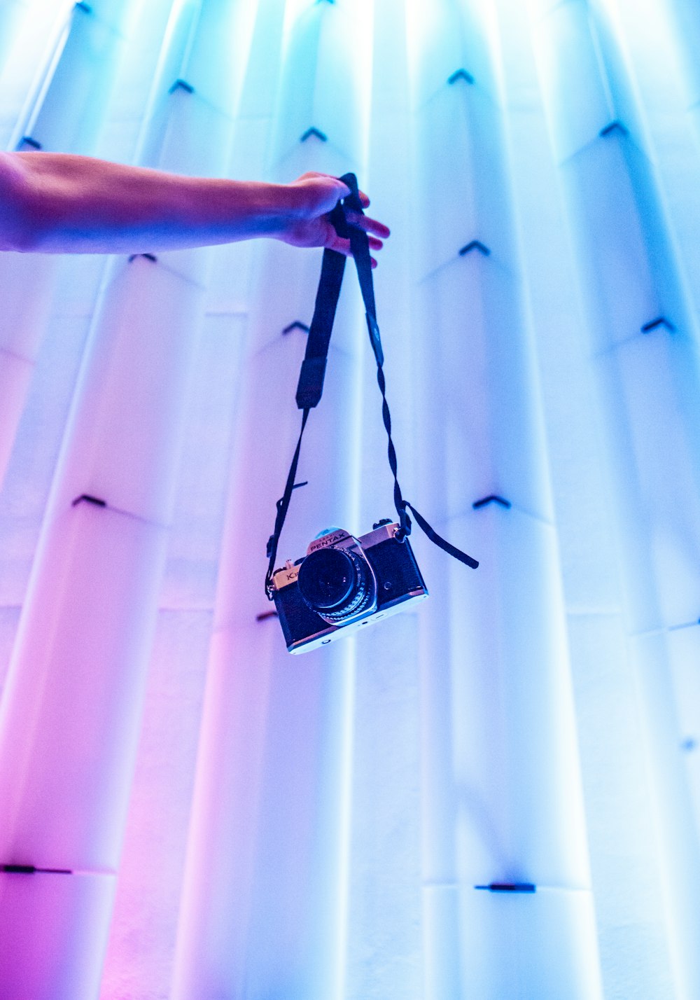 person holding black SLR camera near white curtain