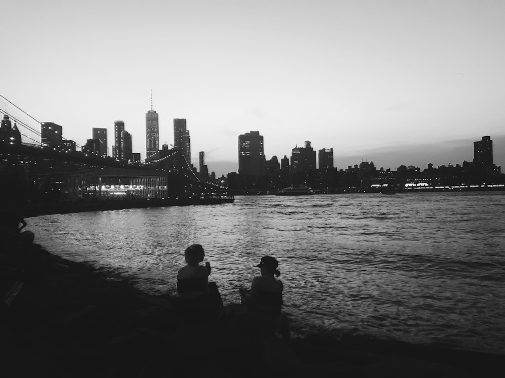 grayscale photo of two women sitting and facing sea